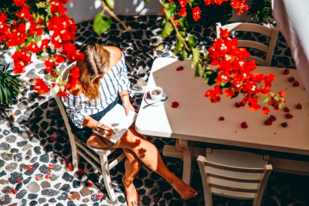 A lady is writing a book seating at the kitchen courtyard with dining table and garden of Mansion sophia heritage villa in Megalochori Santorini